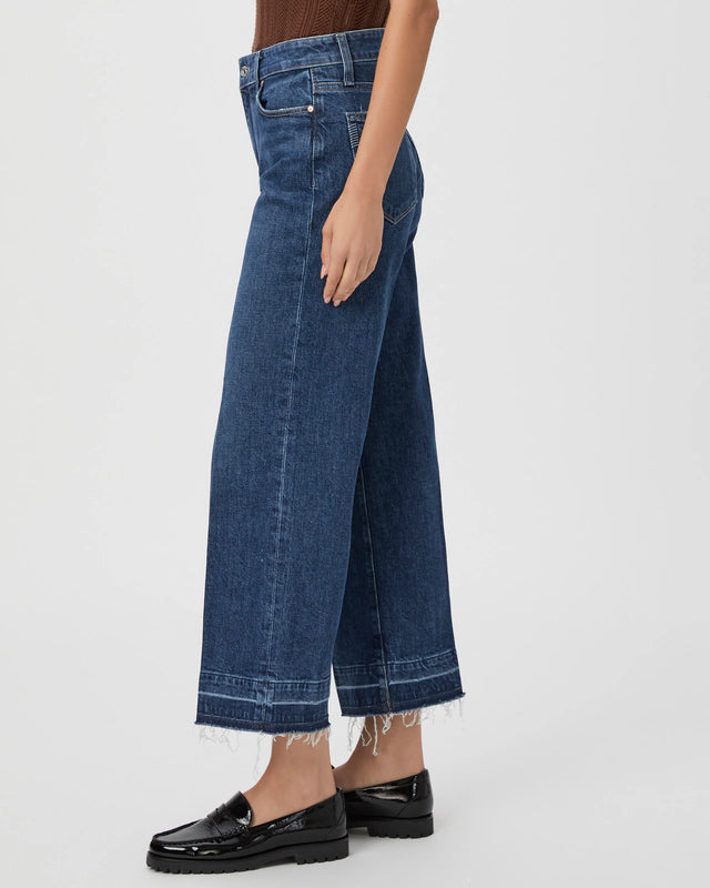 Person wearing Paige's Anessa Wide Leg - Alana jeans, featuring a vintage-inspired, ultra high-waisted design with a frayed hem, and black loafers, standing sideways.