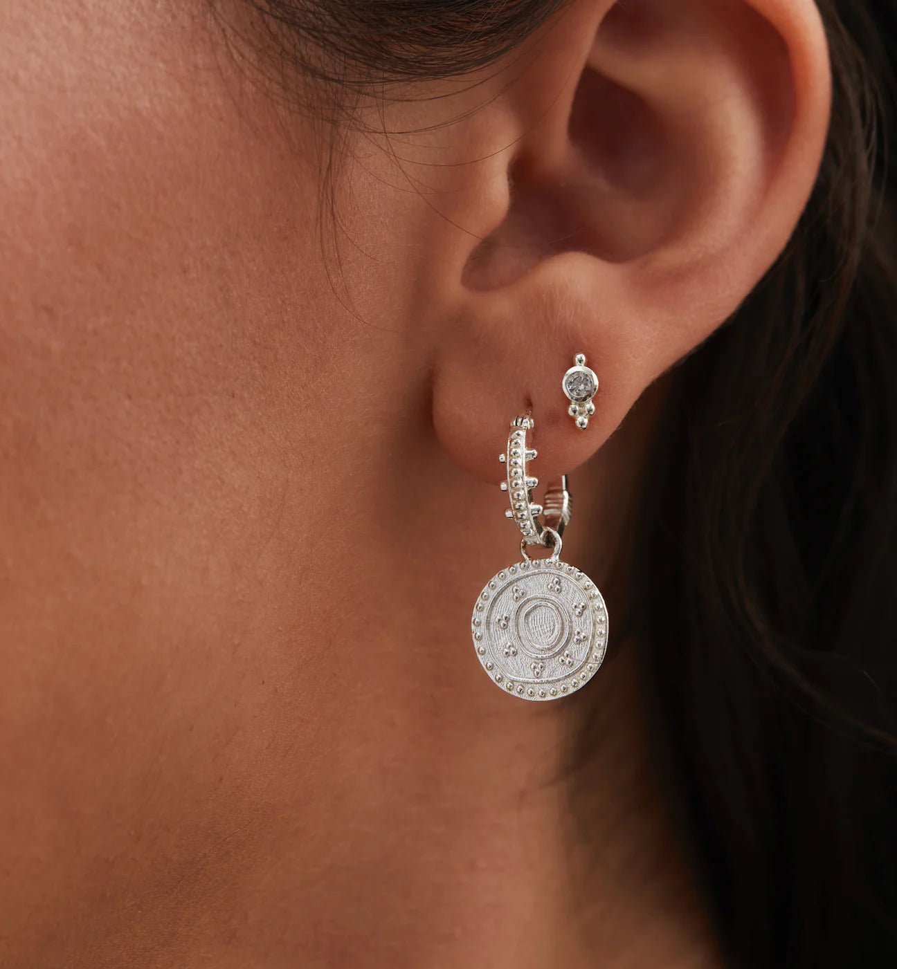 A woman's ear with an Anna + Nina Single Dot Stud - Silver coin and a 925 sterling silver earring.