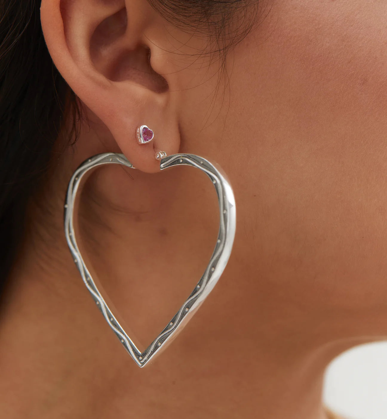 A woman wearing a pair of Anna + Nina Funky Love Hoop Earrings in silver with a classic twist.