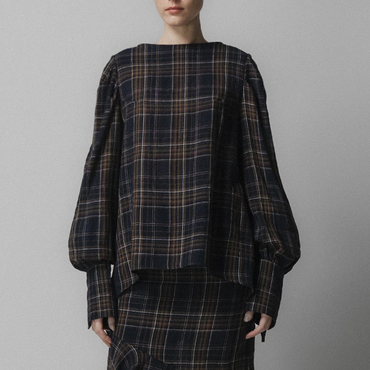 A woman wears the Emin and Paul Volume Sleeve Blouse in navy check, styled with a skirt.