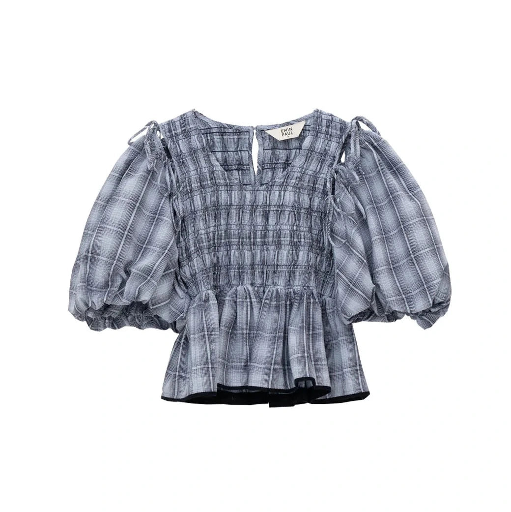 The Emin and Paul Puff Sleeve Tie Blouse - Blue Check is 100% cotton, features a gray plaid pattern, short puff sleeves, a smocked bodice, and ruffled hem, shown on a plain white background.