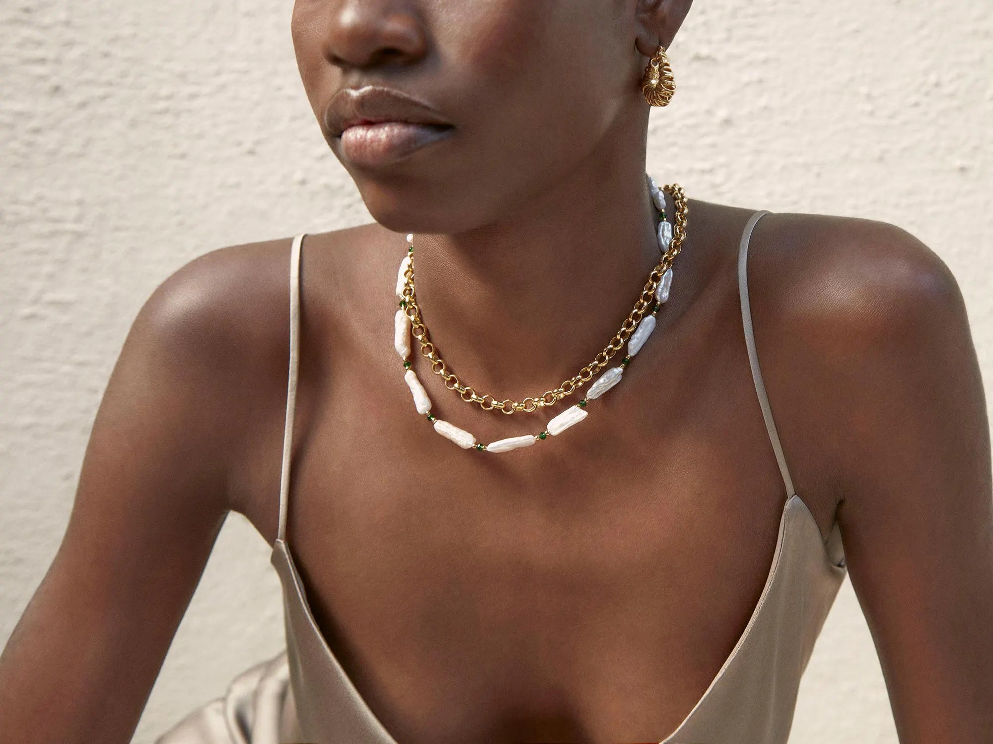 A black woman is sitting on a wall wearing a Shyla Bondi Pearl Necklace adorned with crystals.
