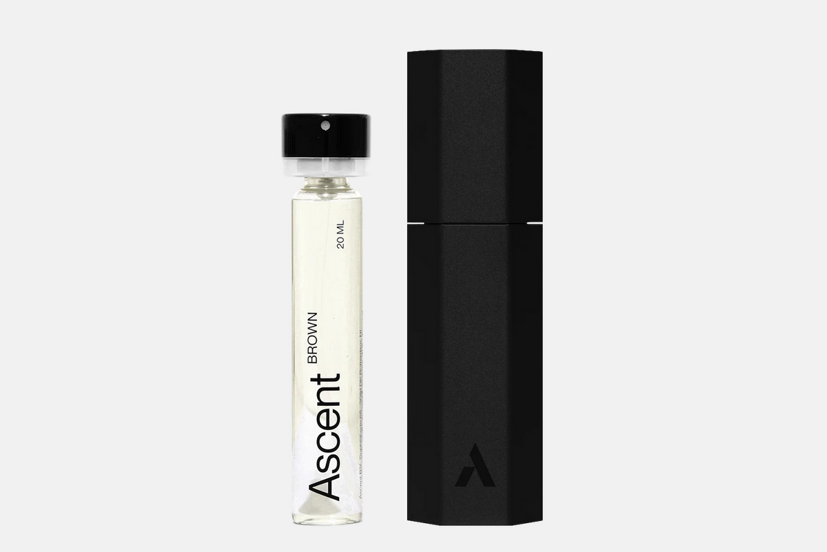A 20 ml glass vial of Ascent Starter Pack - Brown fragrance next to its tall, hexagonal black carrying case.