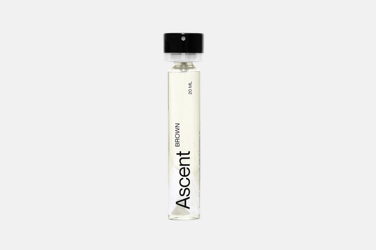 A cylindrical glass vial of Ascent Refillable - Brown perfume with a black cap, labeled “Ascent Brown” and “20 ml.”