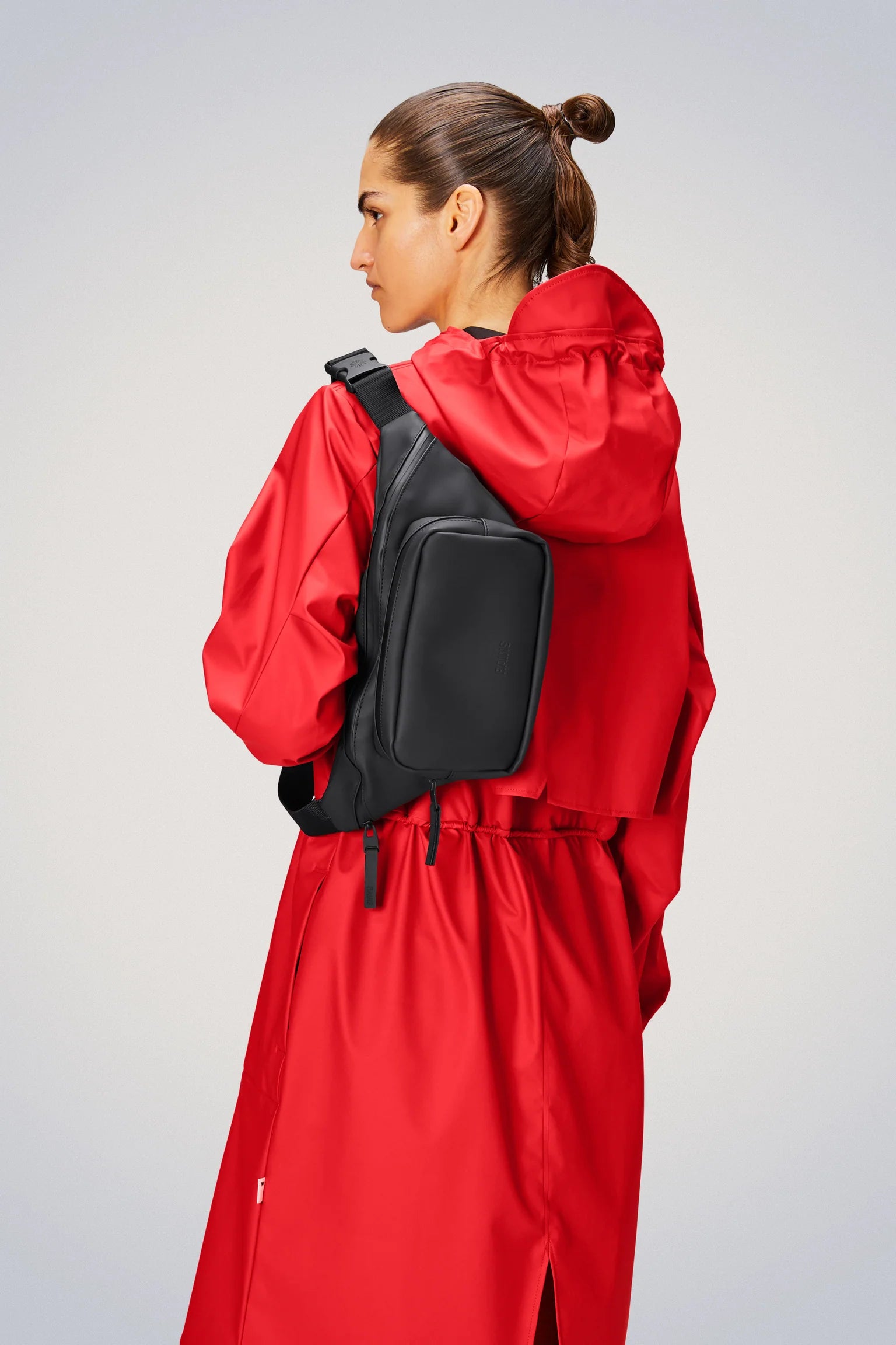 A woman wearing a red raincoat with a Rains Bum Bag - Black.