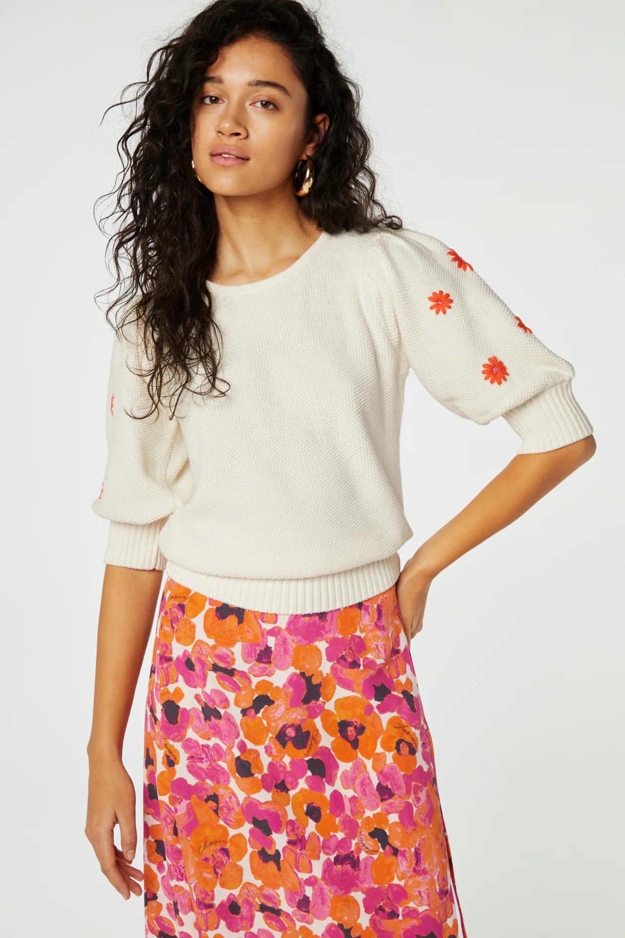 Model wears 3/4 sleeve knit jumper with orange embroidered flowers on sleeves