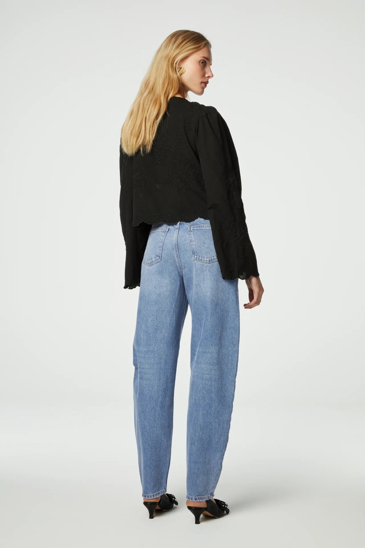 A woman in high waisted jeans showcasing a feminine look from the back wearing the Sterre Top in Black by Fabienne Chapot.