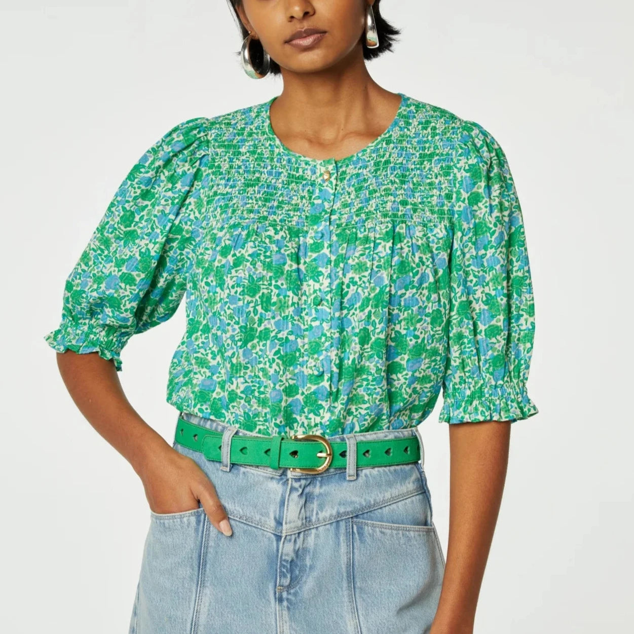 Woman wearing a Fabienne Chapot June Short Sleeve Organic Top in Green Clueless and high-waisted jeans, accessorized with a green belt. Only torso and up shown, against a plain background.