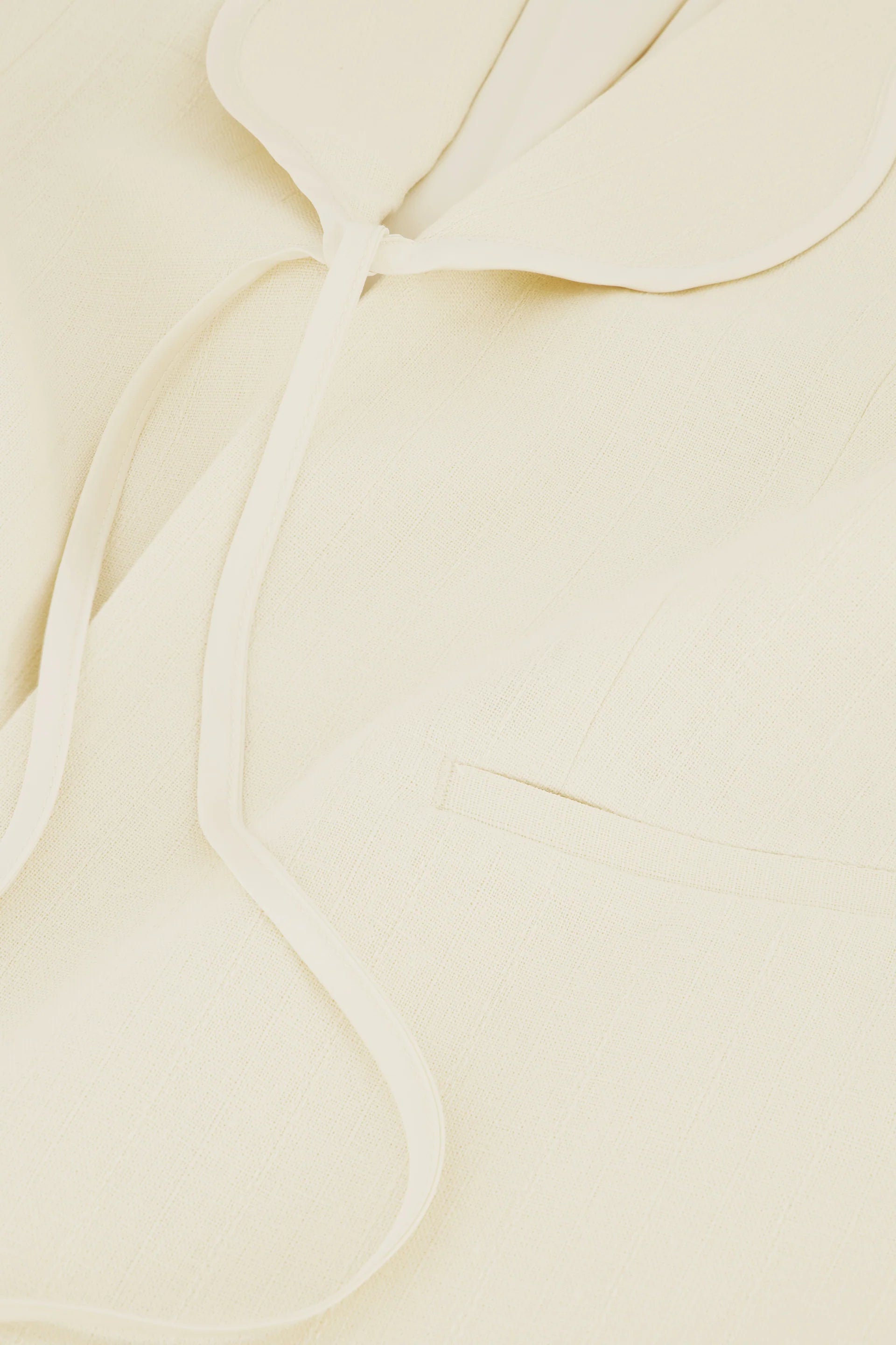 Close-up of the Fabienne Chapot Millor Blazer in Warm White, showcasing its textured linen fabric, notched lapel, slim tie detail, and welt pocket.