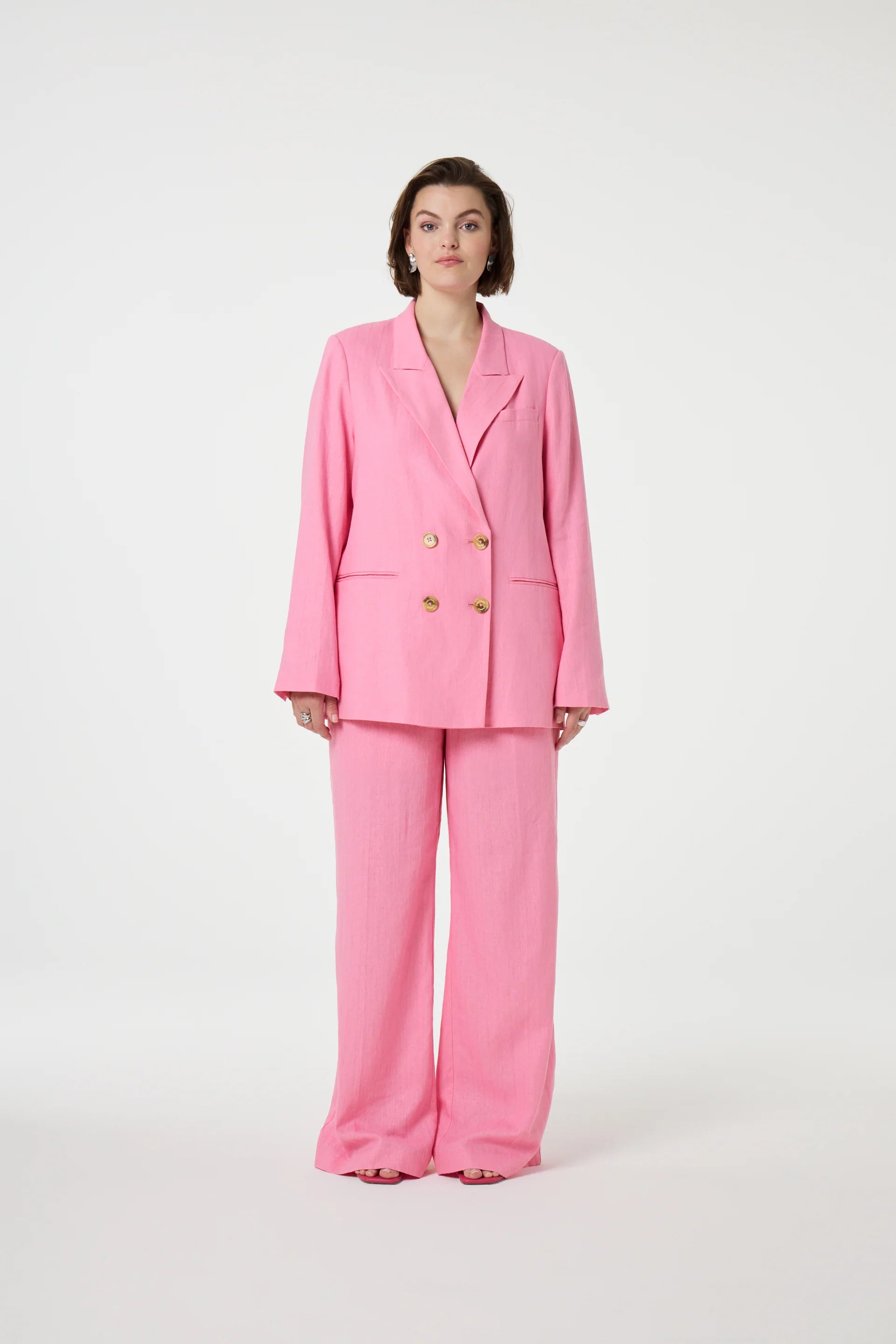 A person faces forward against a plain white background, wearing the Fabienne Chapot Reggy Blazer in Pink Glow with matching wide-leg trousers.