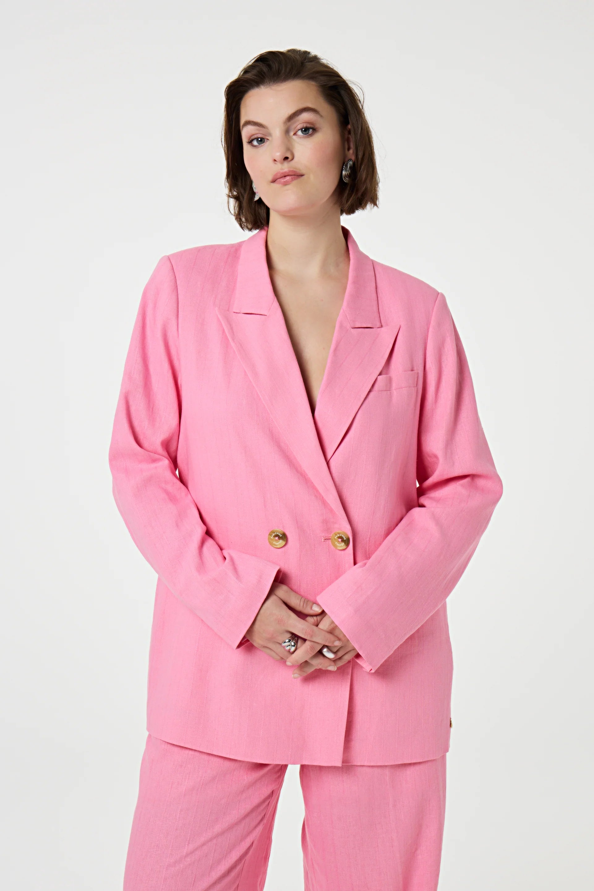 A person with short brown hair wears the Fabienne Chapot Reggy Blazer in Pink Glow, standing against a plain white background with hands clasped in front.