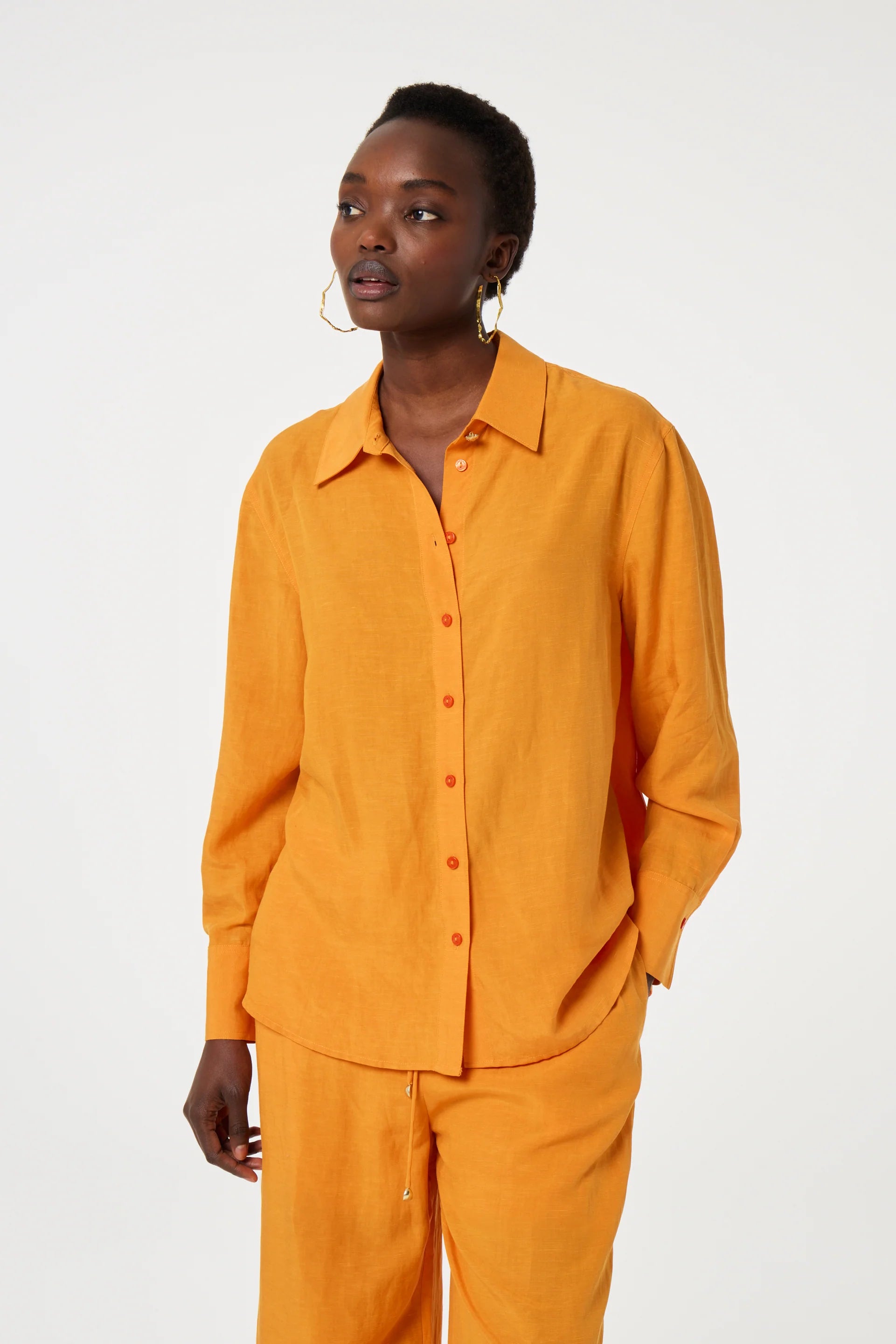 A person wears the Fabienne Chapot Tony Shirt - Jus d'Orange with matching orange pants, standing against a plain light background.