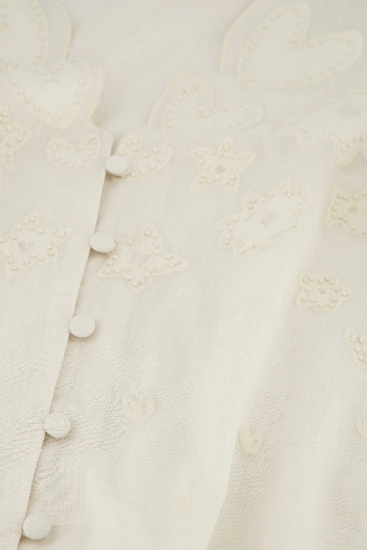 Close-up of the Rani Blouse - Cosy White by Fabienne Chapot, featuring heart and star patterns, vertical buttons, and intricate floral embroidery for an elegant touch.