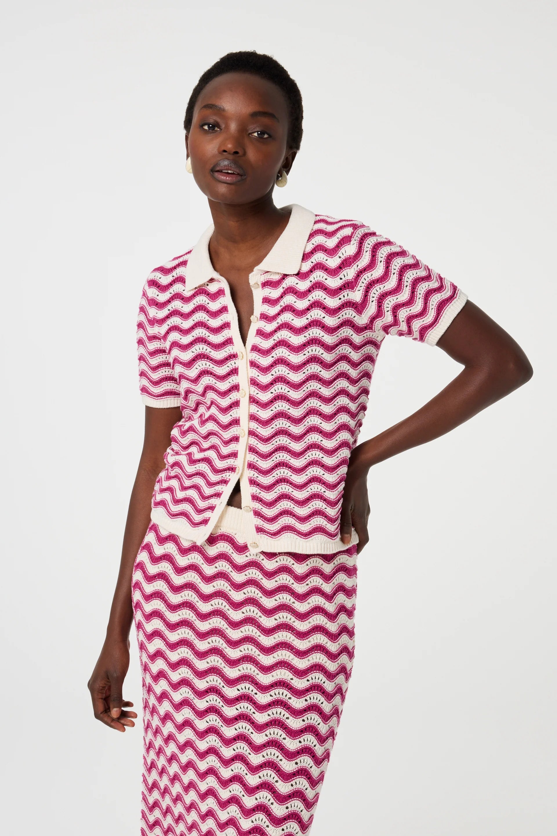 A person wears the Fabienne Chapot Caro Crochet Cardigan in Pink Craze, featuring a pink and white wavy stripe pattern and a cream collar, standing against a plain light background.