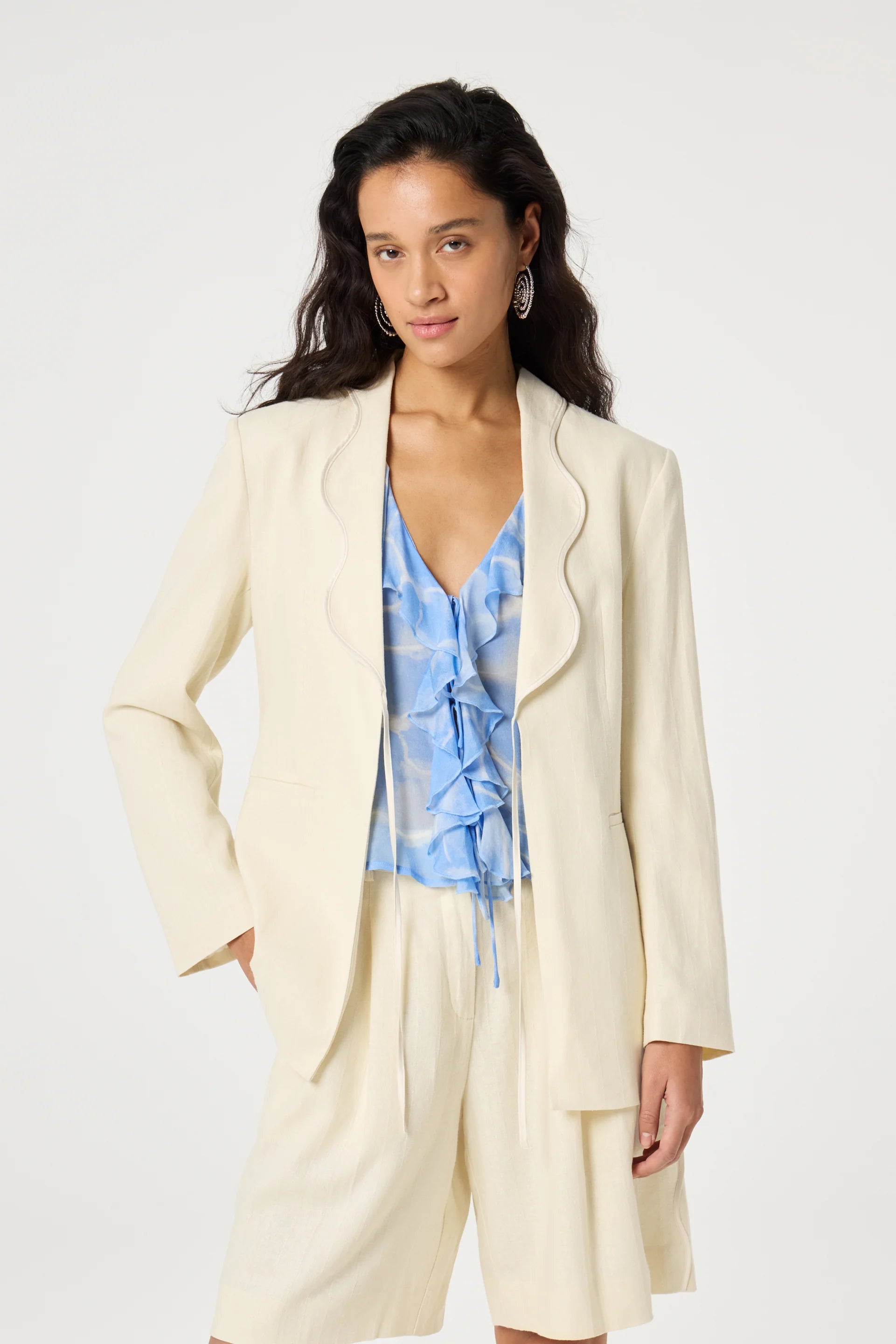 Woman wearing a cream suit with a blue patterned top on a white background
