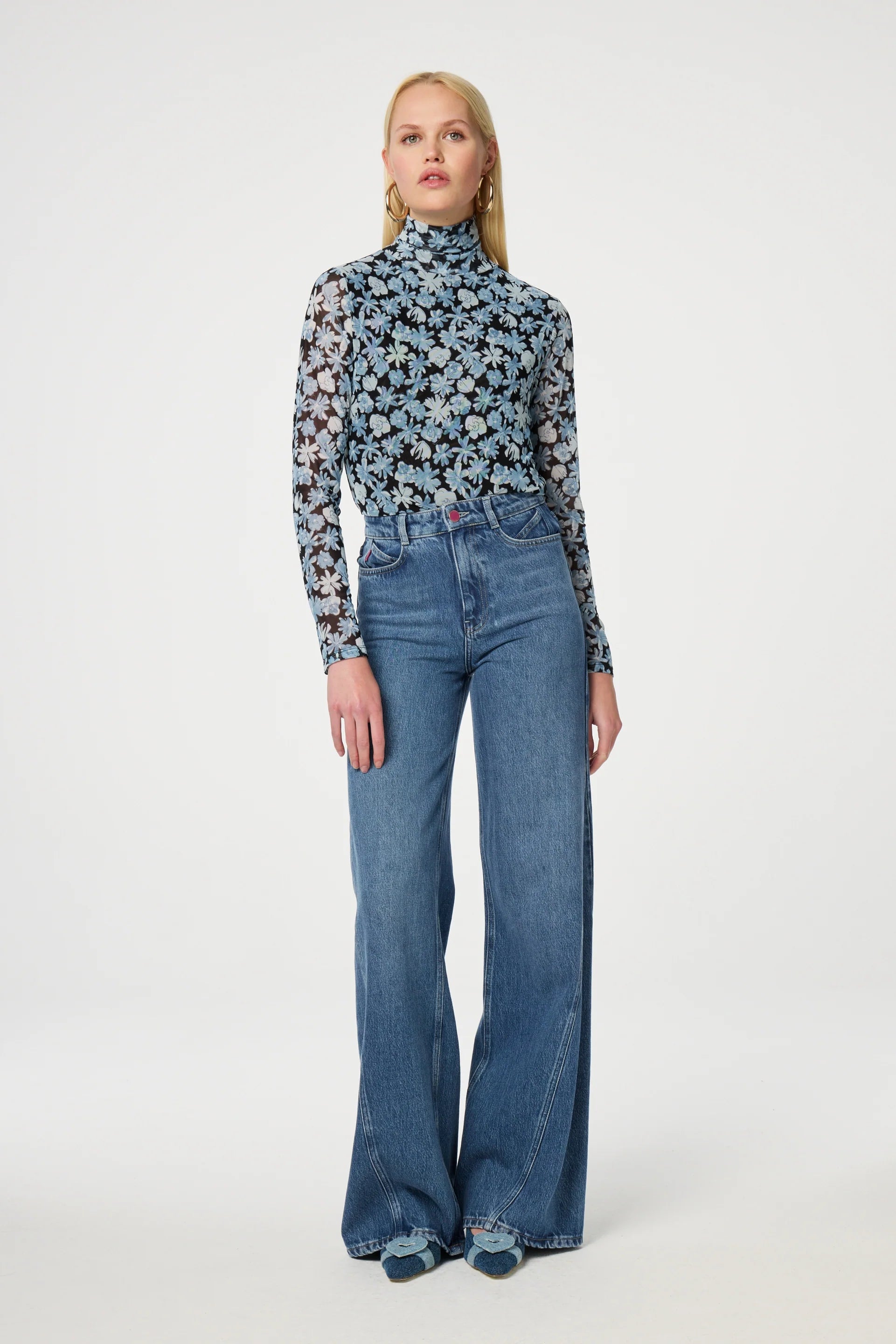 A person stands against a plain background, wearing the Jane Top - Blue Freja by Fabienne Chapot and high-waisted, wide-leg jeans.