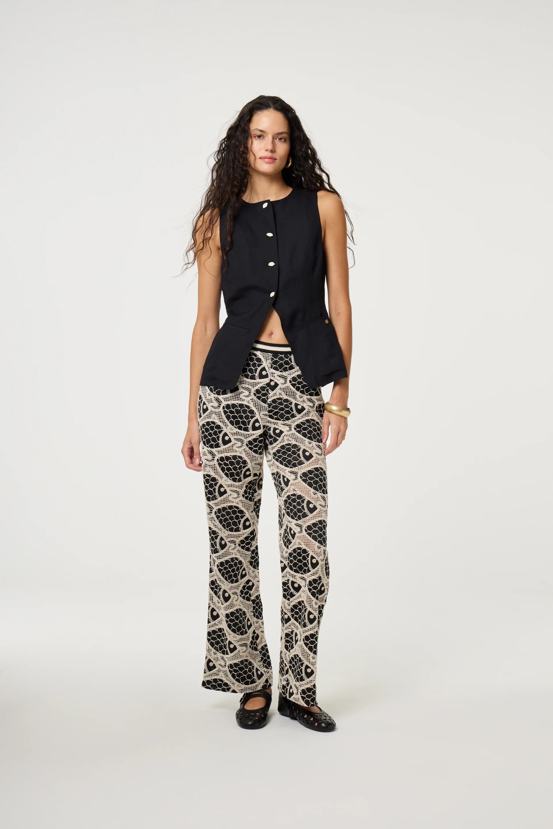 Woman wearing a black sleeveless top and patterned pants on a white background
