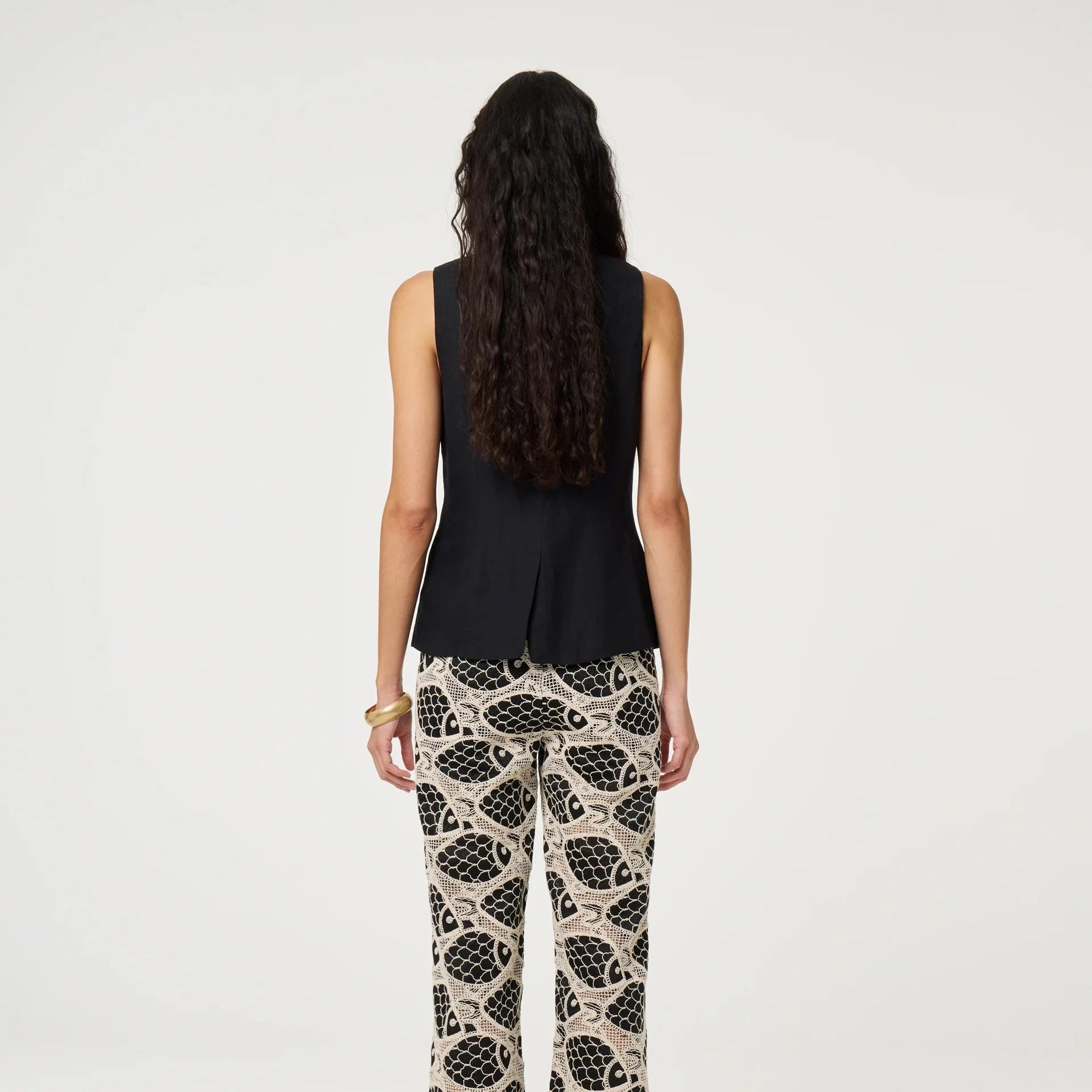 Woman wearing a black sleeveless top and patterned pants on a white background