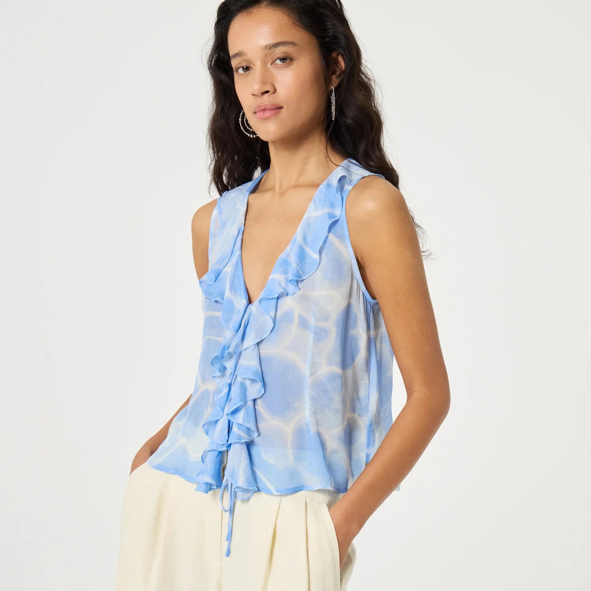 Woman wearing a blue floral sleeveless top and cream shorts on a white background