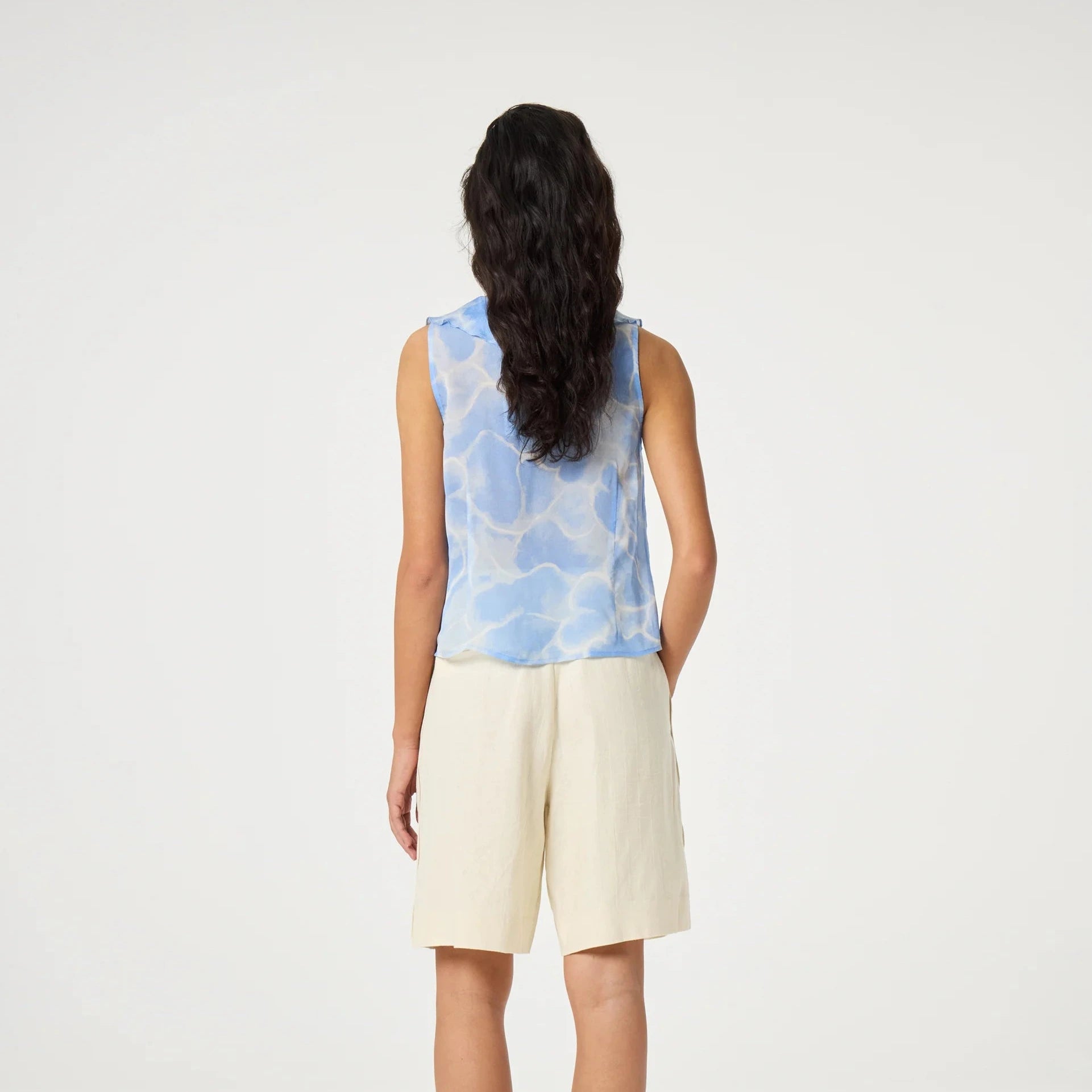Person wearing a sleeveless blue and white patterned top with beige shorts on a white background