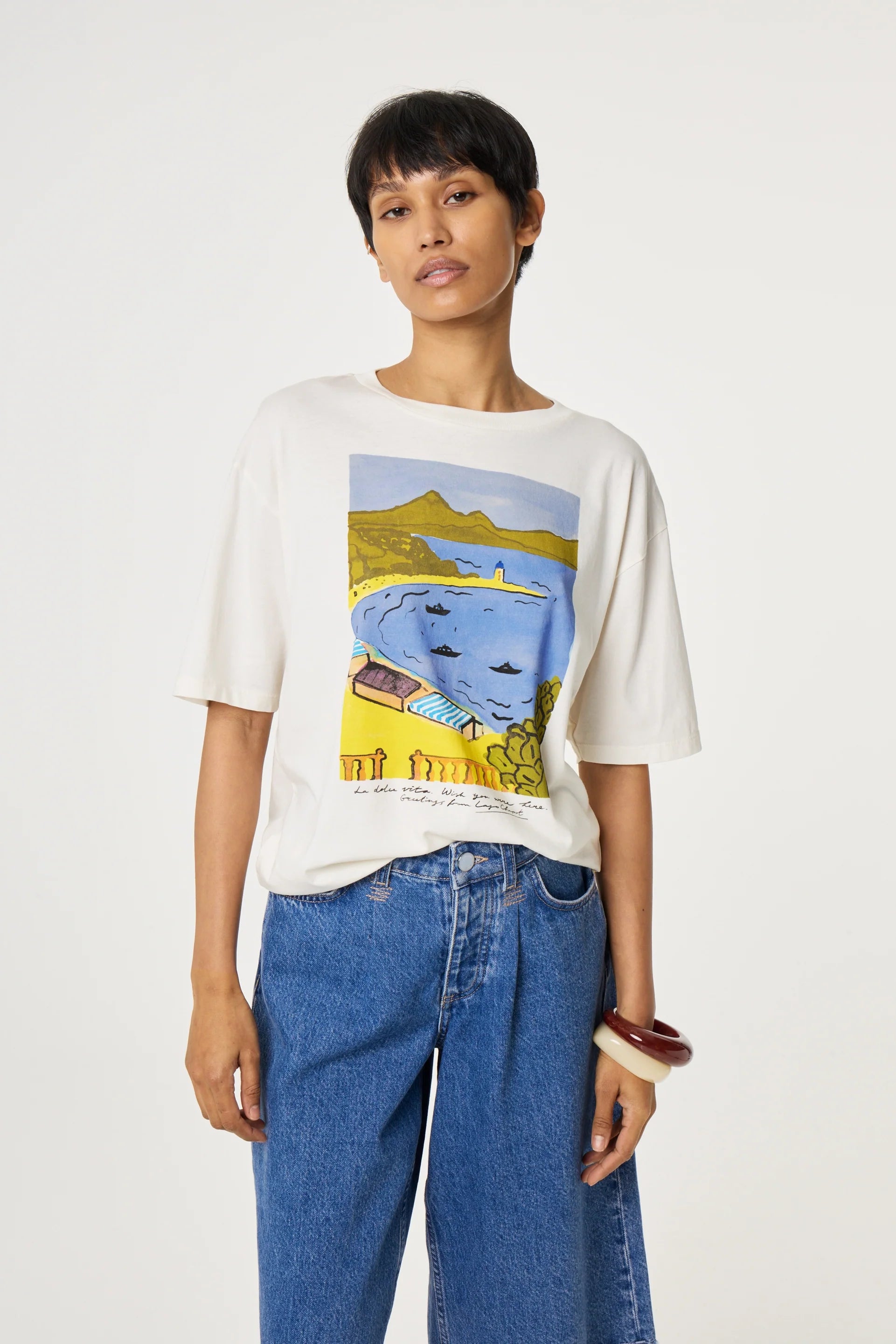 Person wearing a white t-shirt with a colorful graphic design on a plain background fabienne chapot