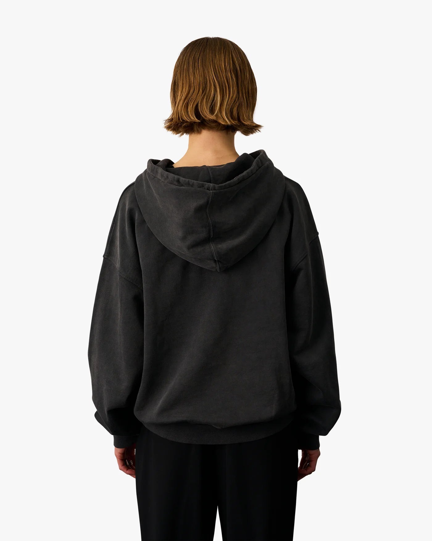 Person with shoulder-length hair wearing the Colorful Standard Organic Oversized Hood in Faded Black made from organic cotton, photographed from the back against a light background.