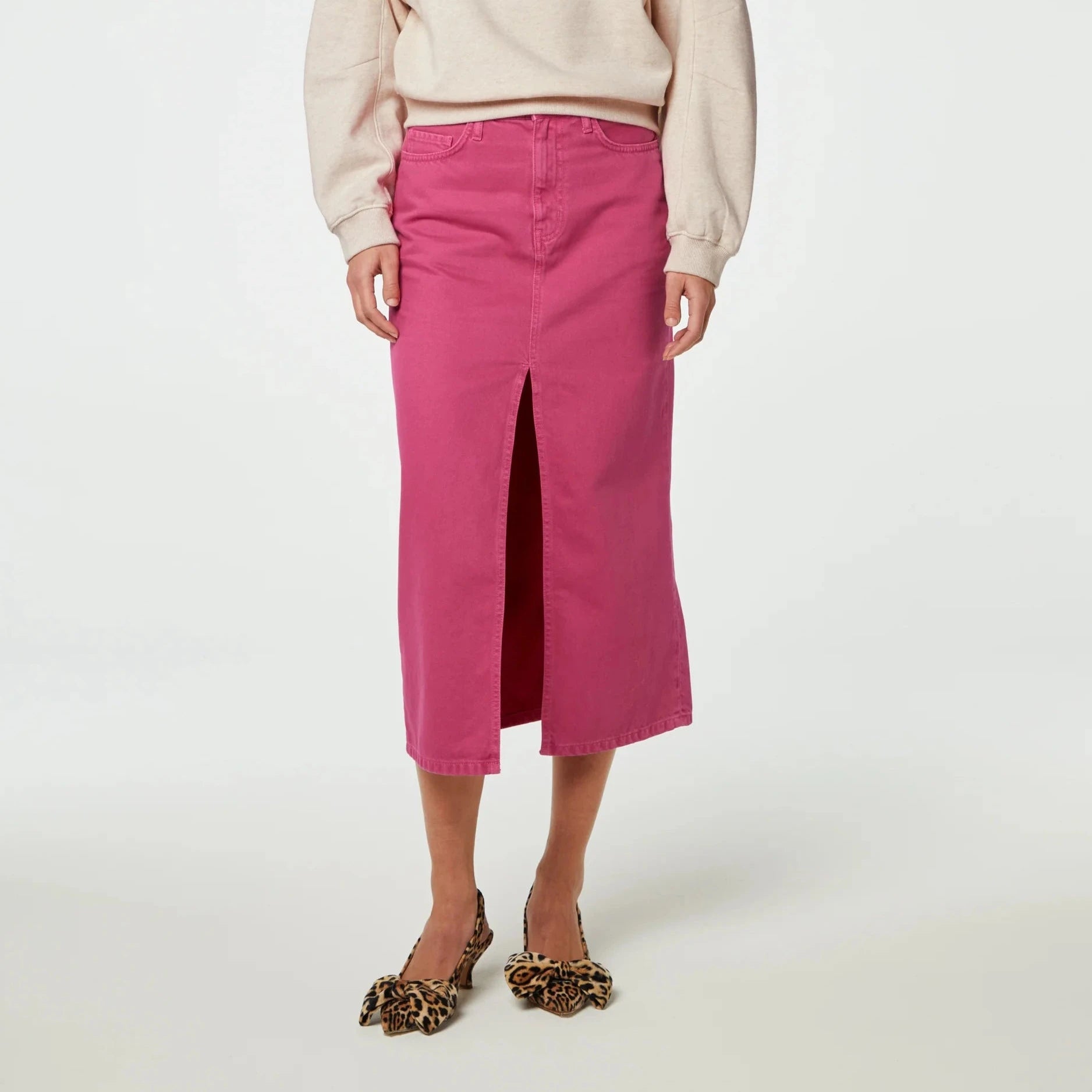 Woman modeling a casual outfit featuring a beige sweatshirt, midi denim Carlyne Skirt in hot pink, and leopard print shoes has been updated to: Woman modeling a casual outfit featuring a beige sweatshirt, midi denim Carlyne Skirt in hot pink by Fabienne Chapot.