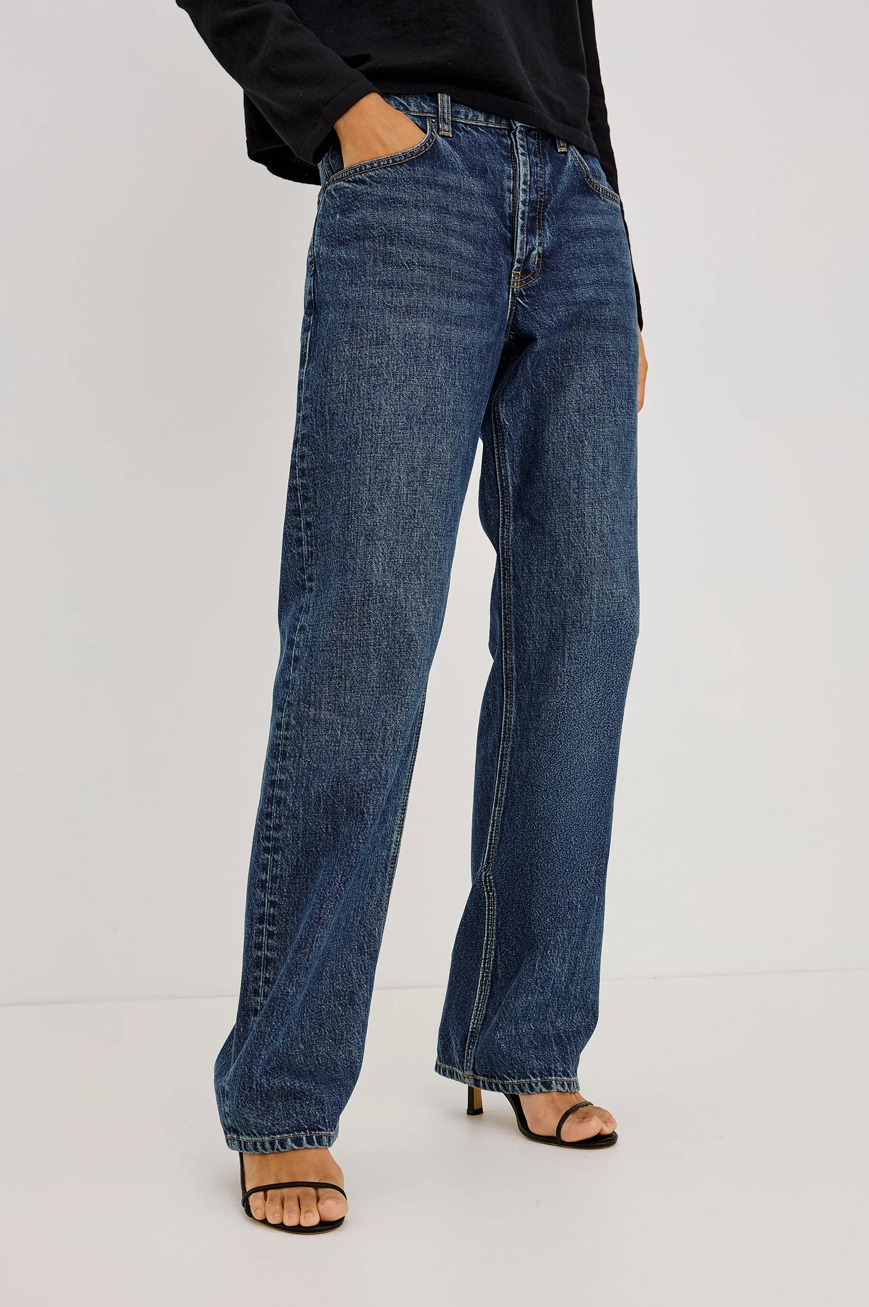 Wearing Rails’ The Del Mar - Upstream relaxed wide-leg blue jeans, a black long-sleeve shirt, and black open-toe heeled sandals, the person stands against a plain light background.