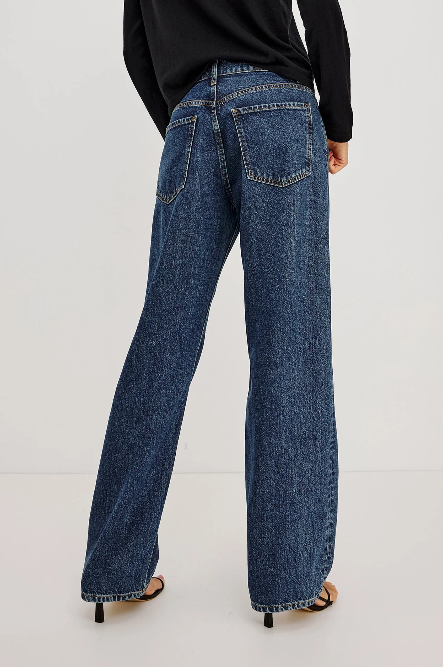Model wears The Del Mar - Upstream relaxed wide-leg jeans by Rails in a classic blue wash and a black long-sleeve top, standing with their back to the camera against a plain white background.
