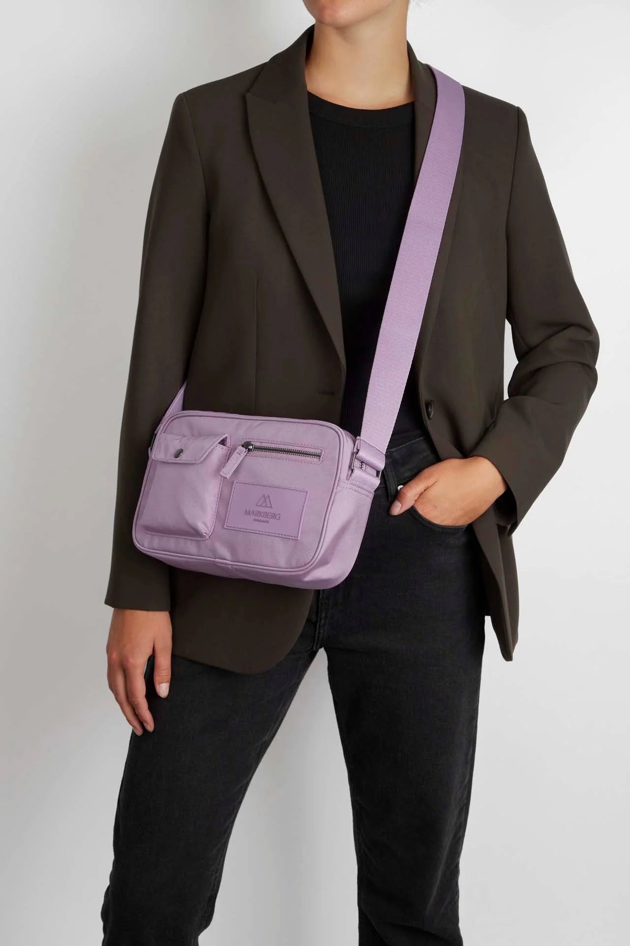 A woman standing with a Markberg Darla Crossbody Bag in Polar Purple across a dark blazer and jeans outfit.