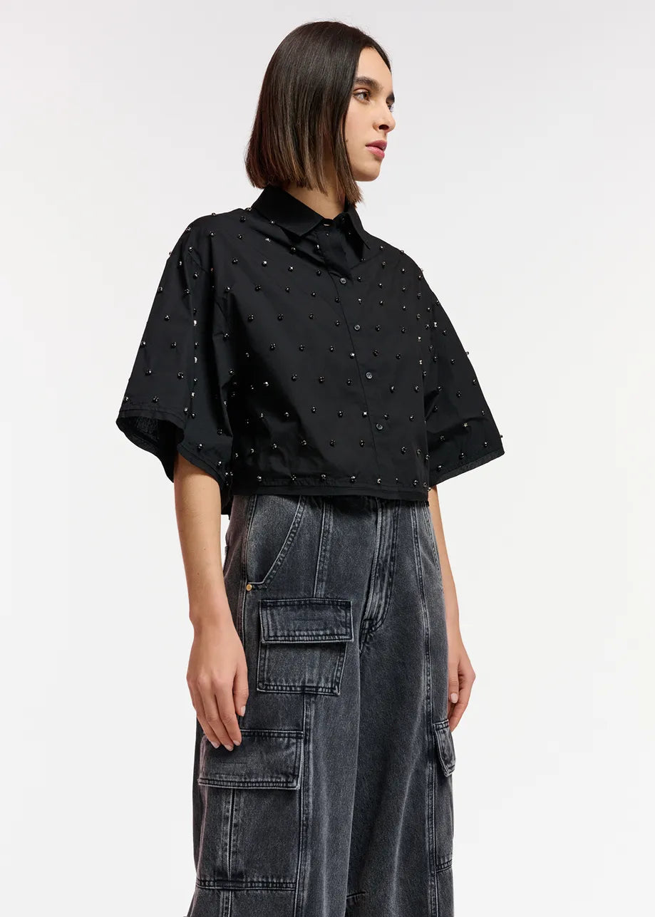 The model is wearing an Essentiel Antwerp black cotton-poplin fabric cropped top and denim cargo pants.