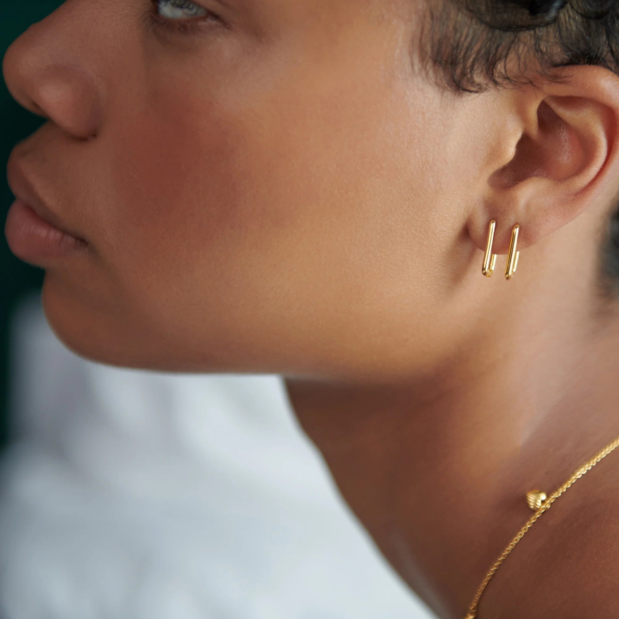 Model wears 2 gold oval hoop earrings.