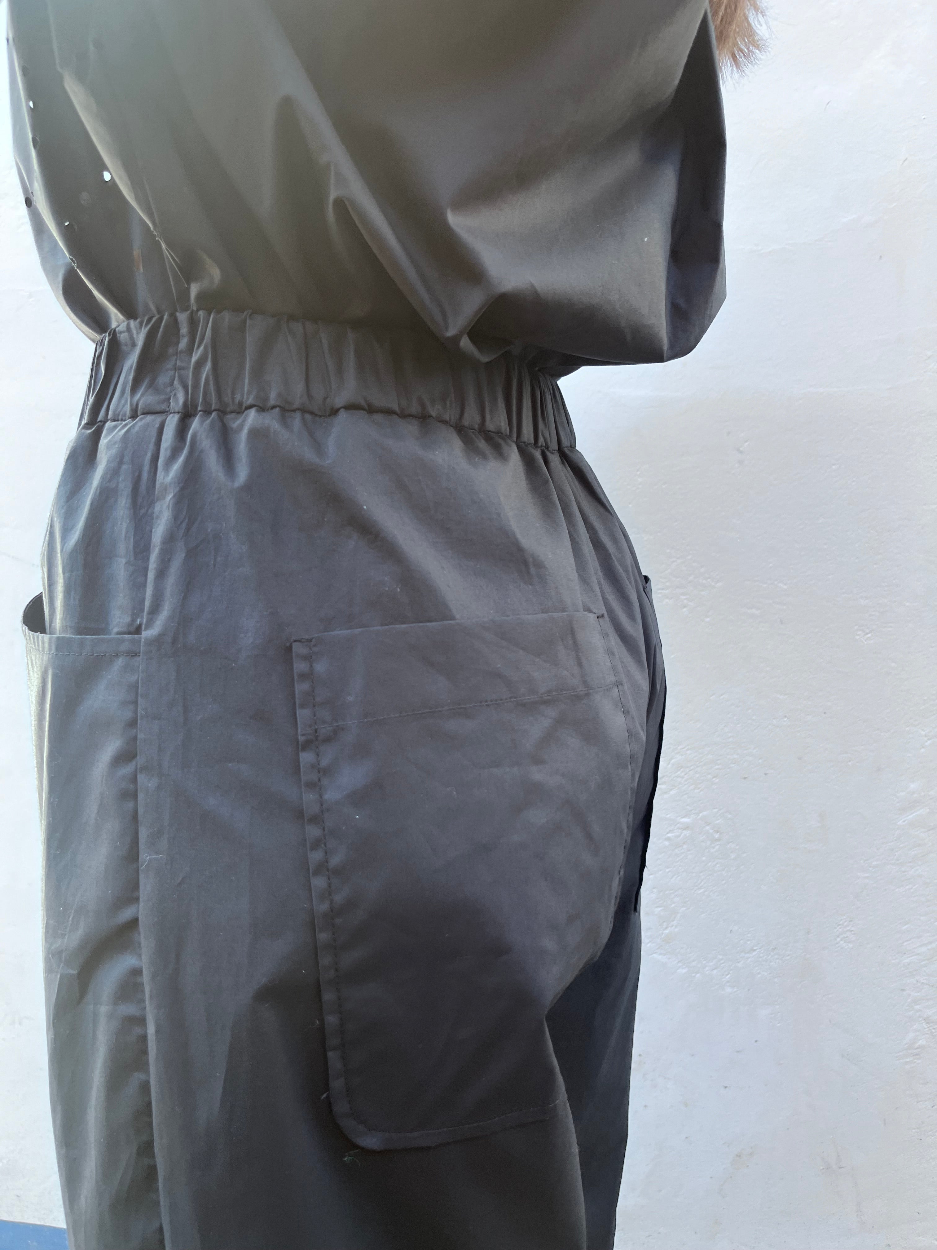 A person wears MeiMeij's Barrel Leg Cotton Trousers in black, featuring silky-soft fabric, an elasticated waistband, and a large side pocket, while standing against a plain light-colored wall.
