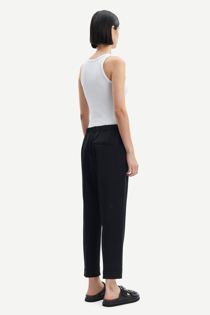 The back view of a woman wearing Samsøe Samsøe black woven trousers with an elasticated waist and a white tank top.