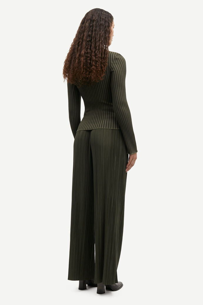 A person with curly hair is wearing the Uma Trousers - Forest Night, a dark green, long-sleeve, pinstriped outfit made from recycled polyester by Samsøe Samsøe, standing and facing away from the camera.