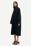 Model wears long coat navy coat with a round neckline and collar and large cuffed sleeves. Side view.