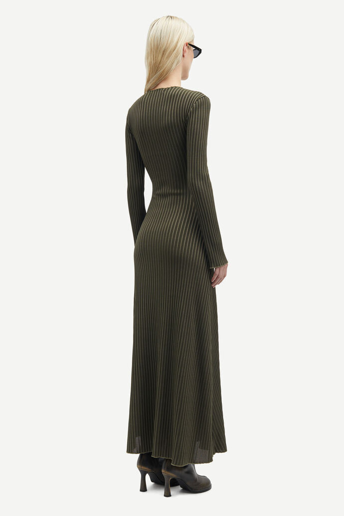 A person with blonde hair is wearing the Samsøe Samsøe Sacrane Maxi Dress in Green Rib and heeled ankle boots, facing away from the camera.