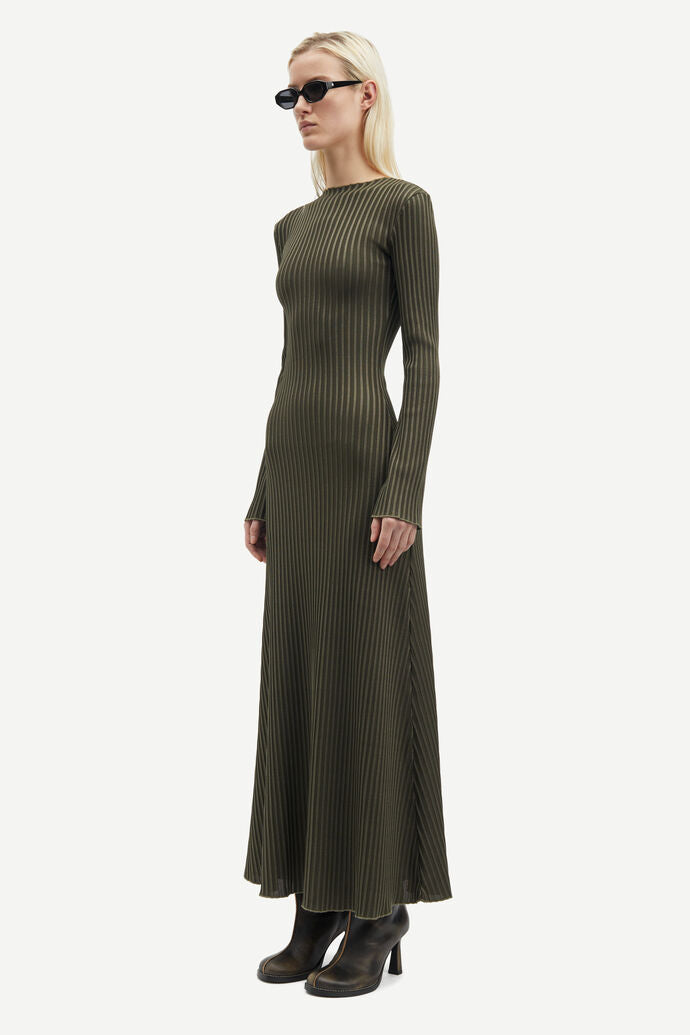 A woman with blonde hair wears dark sunglasses and the long-sleeved, floor-length Sacrane Maxi Dress - Green Rib by Samsøe Samsøe, made from recycled polyester, standing in a neutral pose.