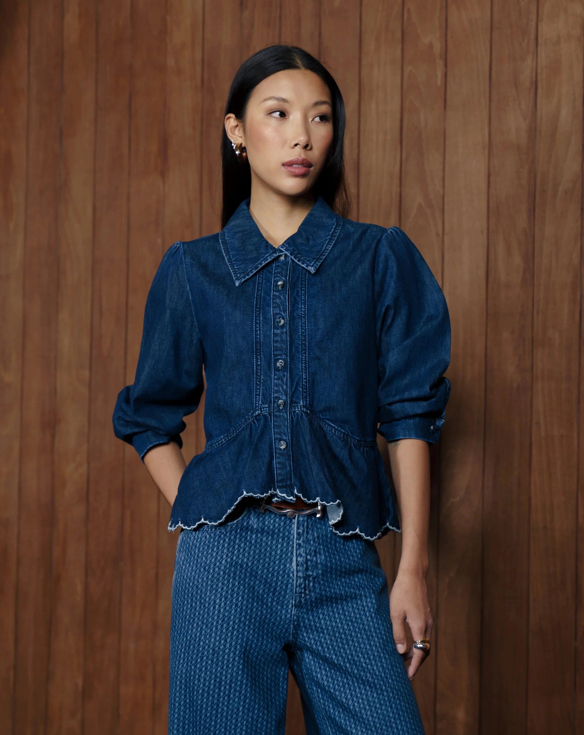 Wearing the Seventy & Mochi Tate Blouse - Americana, a person stands in front of a wooden wall paired with blue jeans.