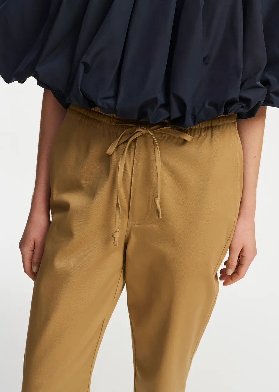 Model wears tapered trousers with turned hem in camel shade