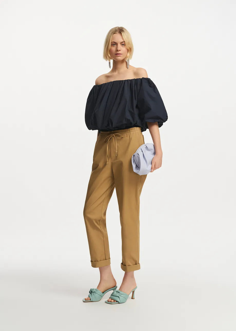 Model wears tapered trousers with turned hem in camel shade