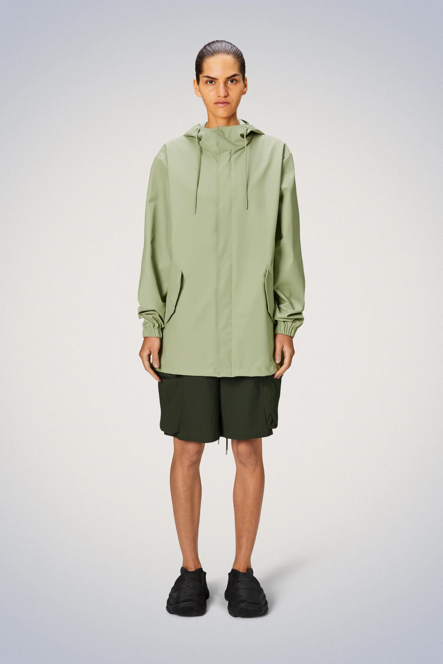 A man donning a Rains Fishtail Jacket in a vivid shade of green, exuding a pared-back aesthetic.