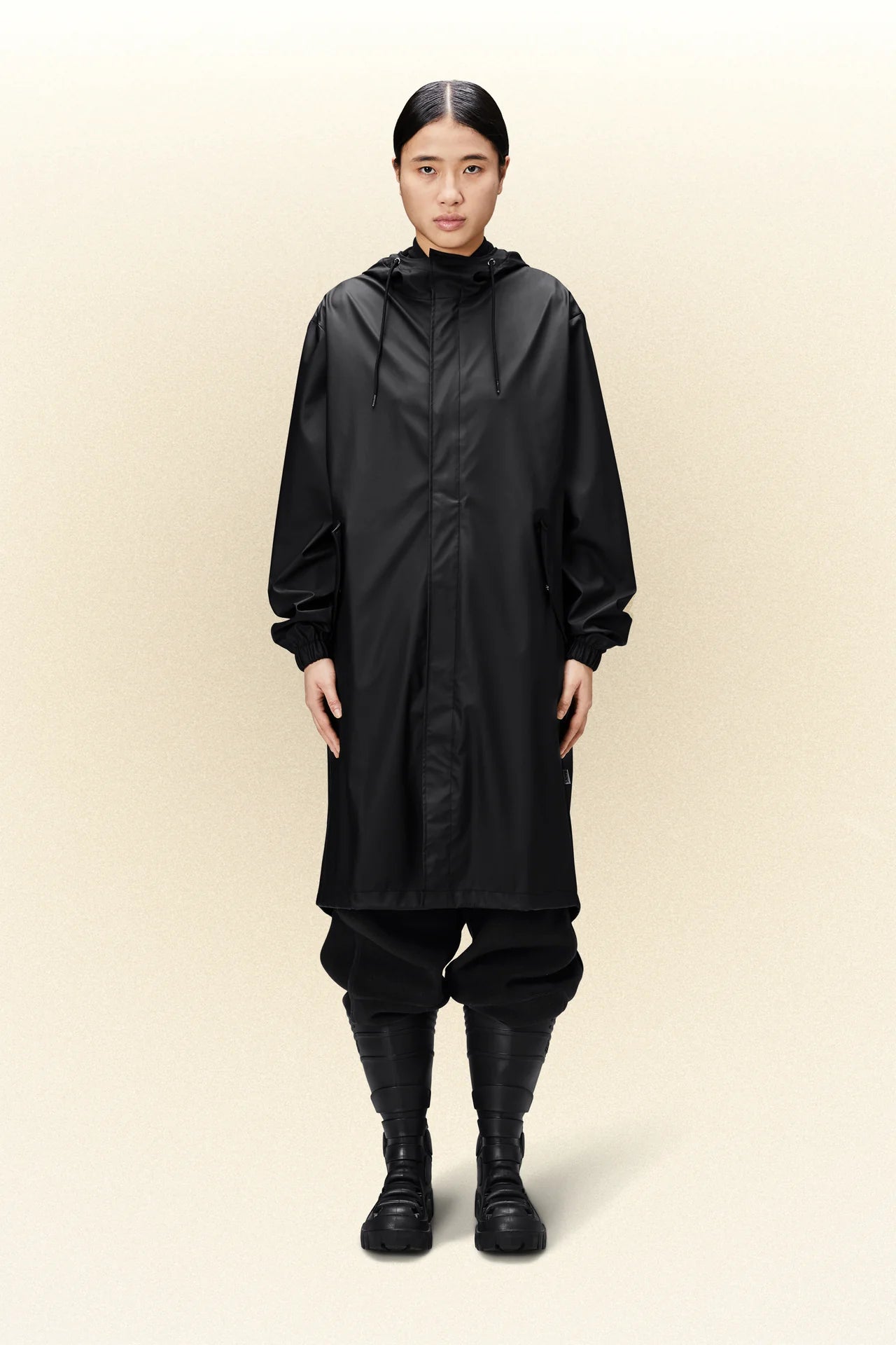 Description: A woman wearing a lightweight black Rains fishtail parka and waterproof boots.