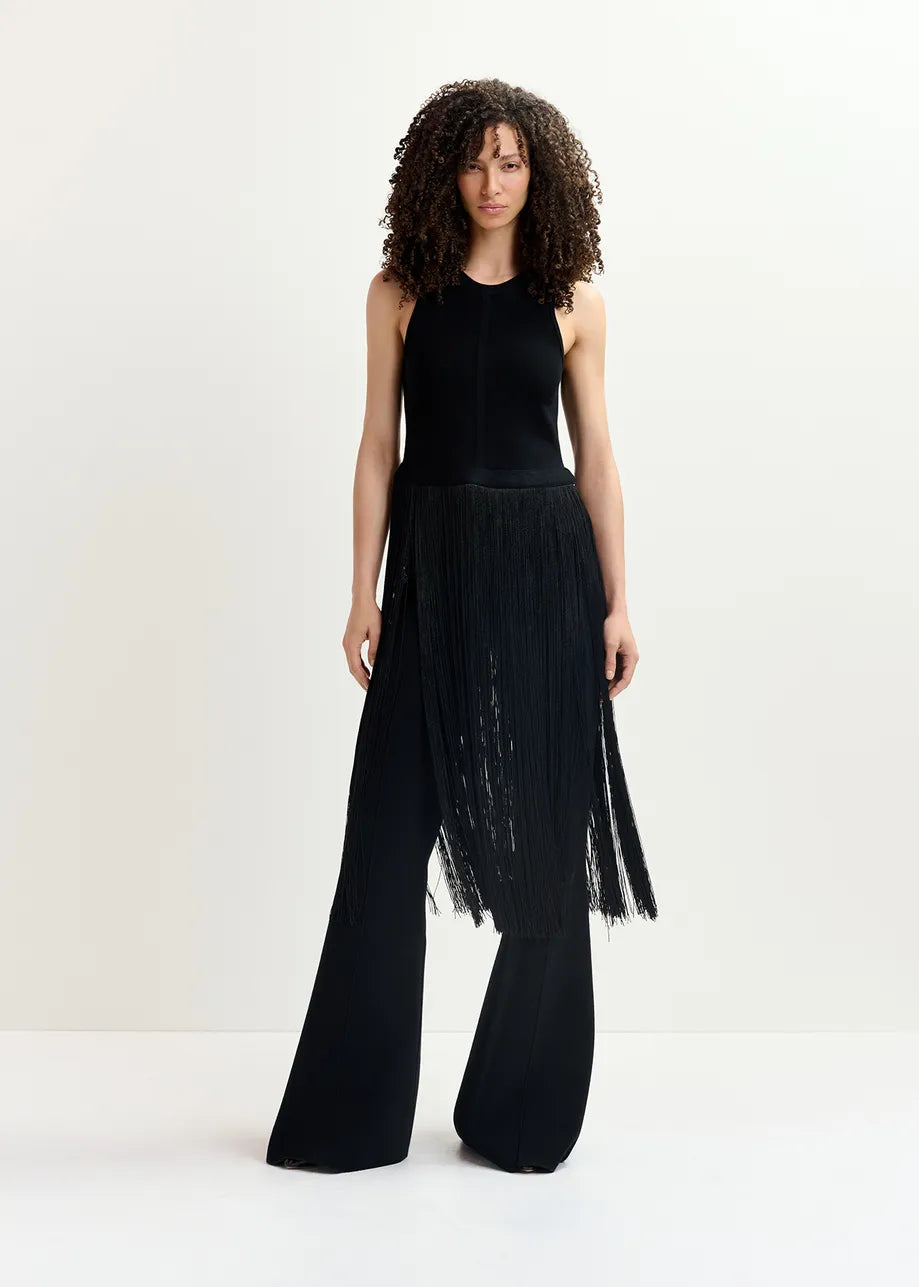 A woman stands against a plain background wearing the Gabbers Fringed Top in black from Essentiel Antwerp and wide-leg pants with fringed details.