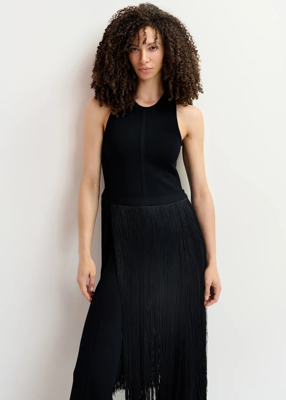 A person with curly hair wearing the Gabbers Fringed Top - Black by Essentiel Antwerp stands against a plain white background. The sleeveless, slim fit top features long fringes that add dynamic movement to the sleek silhouette.