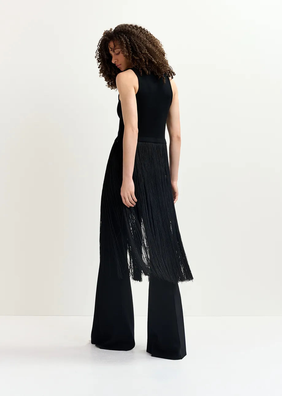 A person with curly hair stands facing away, showcasing the Essentiel Antwerp Gabbers Fringed Top - Black, paired with wide-legged pants and a sleeveless knitted top.