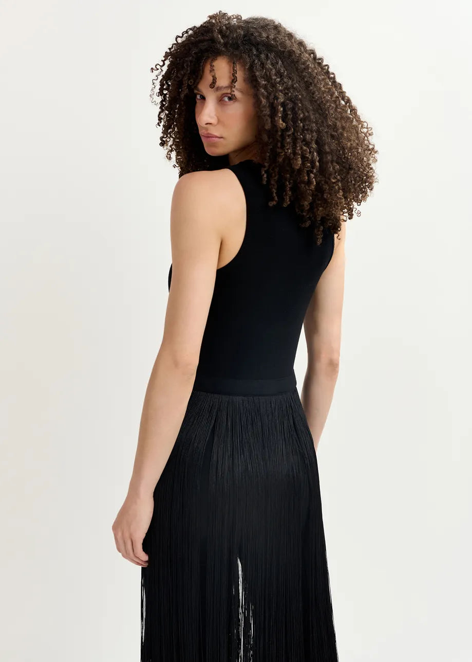 A person with curly hair is wearing the Essentiel Antwerp Gabbers Fringed Top in black, facing slightly away and looking over their shoulder.