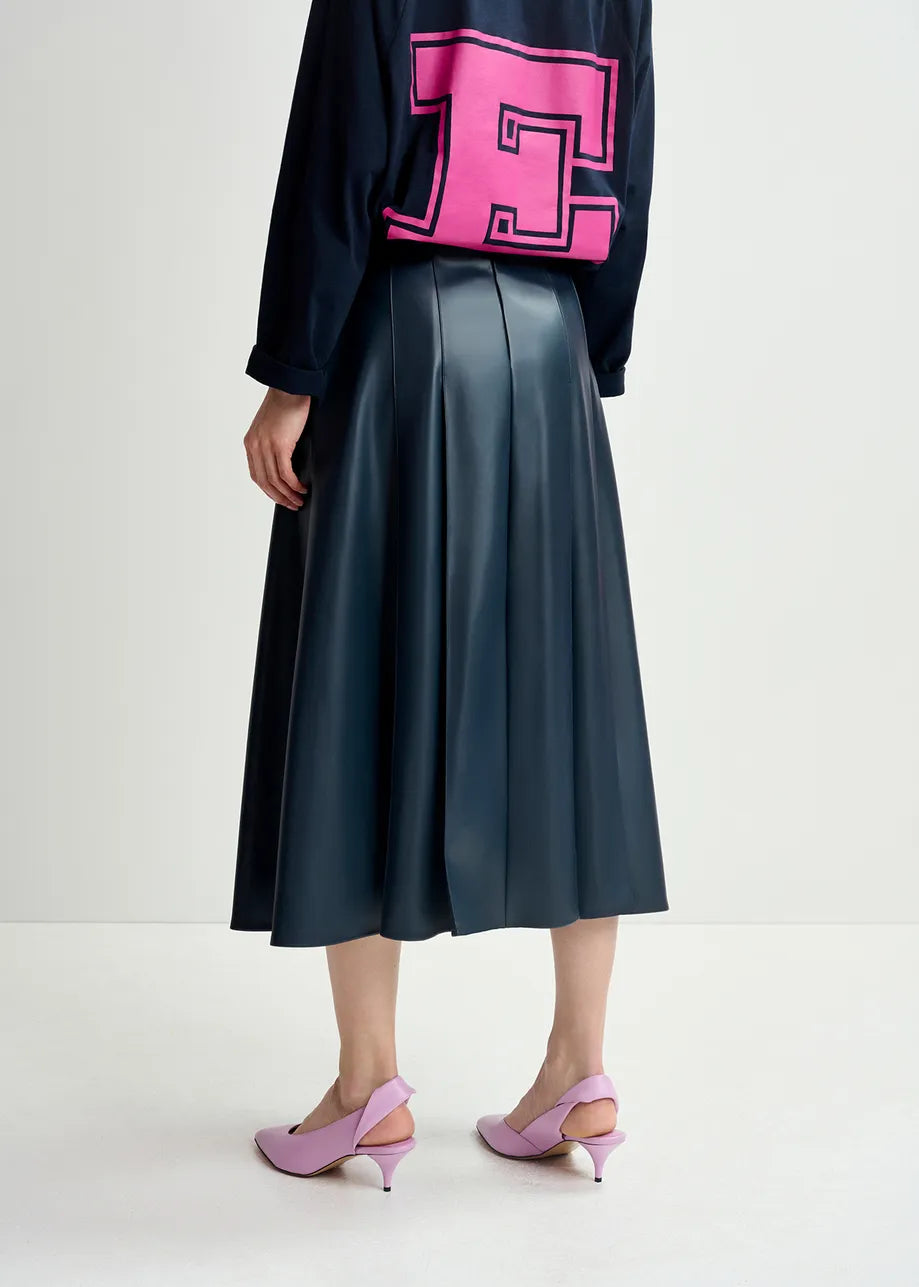 Person wearing a black top with a large pink "F" on the back, an Essentiel Antwerp Geeuw Faux Leather Skirt in Navy, and pink heeled shoes, standing against a plain background.