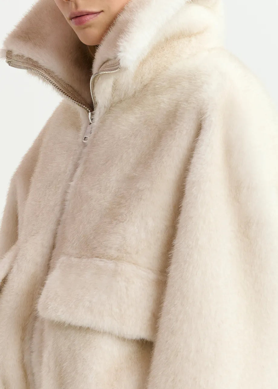 Close-up of a person wearing a white fuzzy faux fur Genz Bomber Jacket with a high collar and front zipper from Essentiel Antwerp. The person's face is partially visible, turned slightly to the side, emphasizing how this oversized silhouette adds a trendy touch to their look.