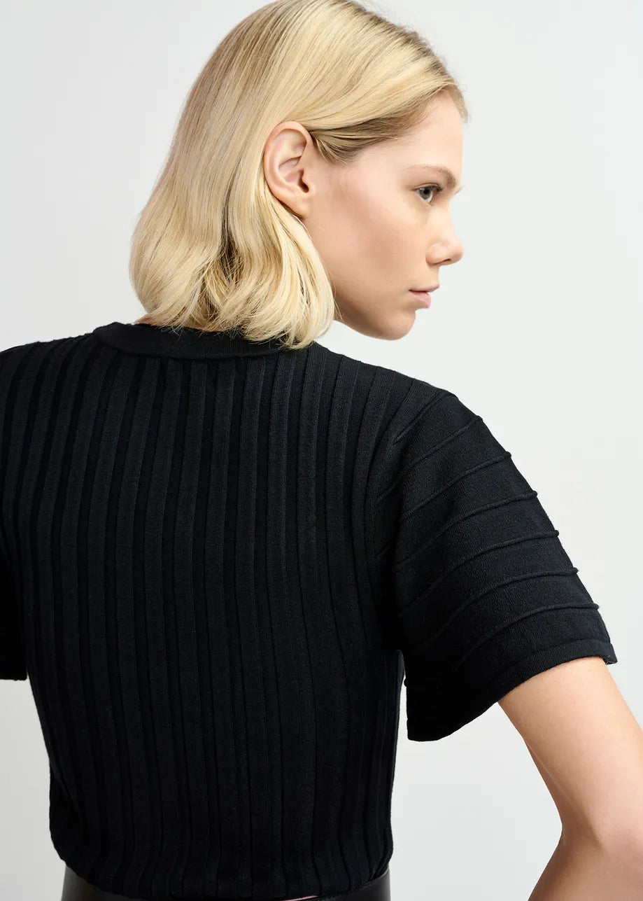 A person with short blond hair is shown from the side wearing a black Georgie rib-knitted top from Essentiel Antwerp.